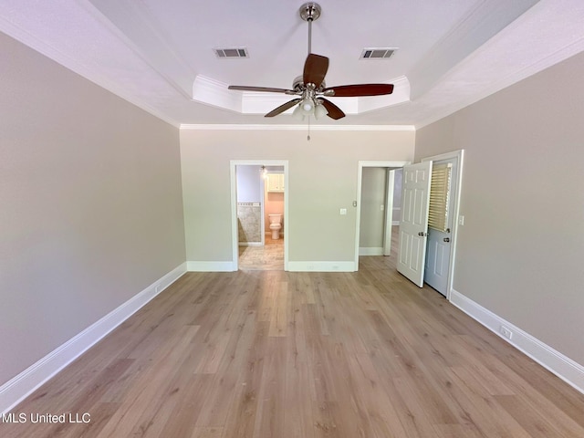 unfurnished bedroom featuring baseboards, ornamental molding, light wood-style floors, visible vents, and a raised ceiling