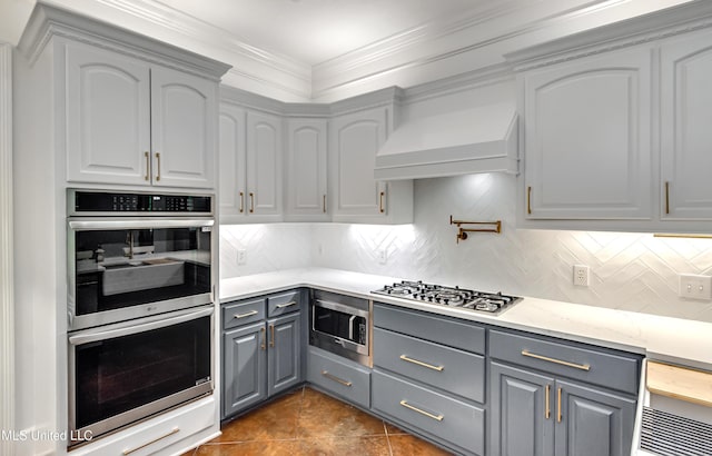 1025 Monet Cv, Brandon, MS 39047 - kitchen with gray cabinetry, appliances with stainless steel finishes, premium range hood, backsplash, and dark tile patterned flooring