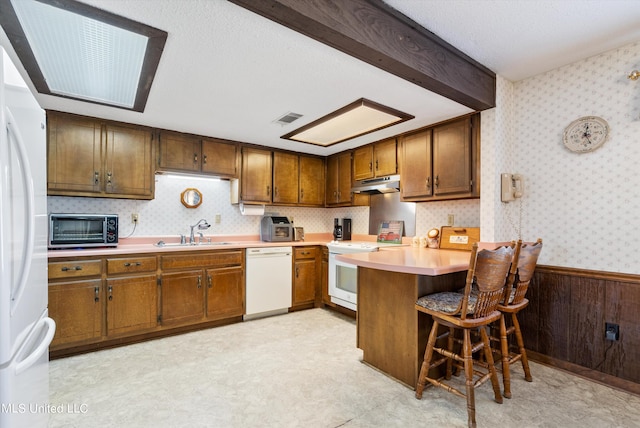 kitchen featuring kitchen peninsula, sink, a breakfast bar, white appliances, and wood walls