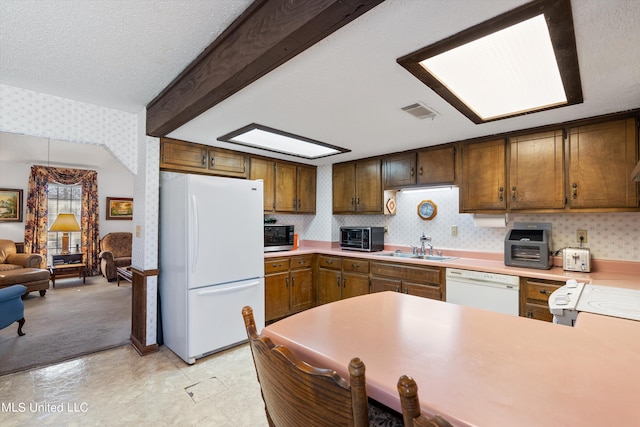 kitchen with kitchen peninsula, beam ceiling, a textured ceiling, sink, and white appliances