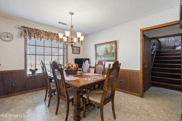 dining area with a textured ceiling, a chandelier, and wooden walls