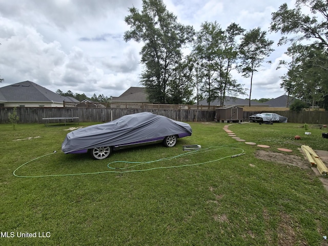view of yard with a trampoline, an outdoor structure, a fenced backyard, and a storage unit