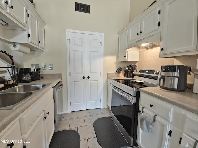 kitchen with under cabinet range hood, light tile patterned floors, a towering ceiling, white cabinets, and appliances with stainless steel finishes
