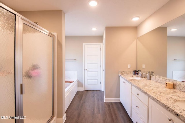 full bath with double vanity, a bath, a stall shower, and wood finished floors