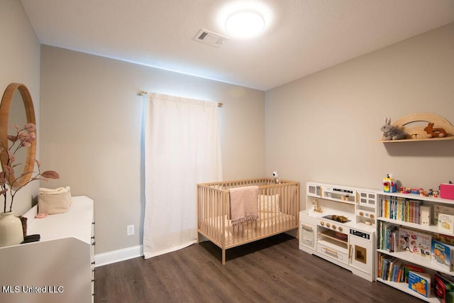 bedroom with baseboards, visible vents, a crib, and dark wood finished floors