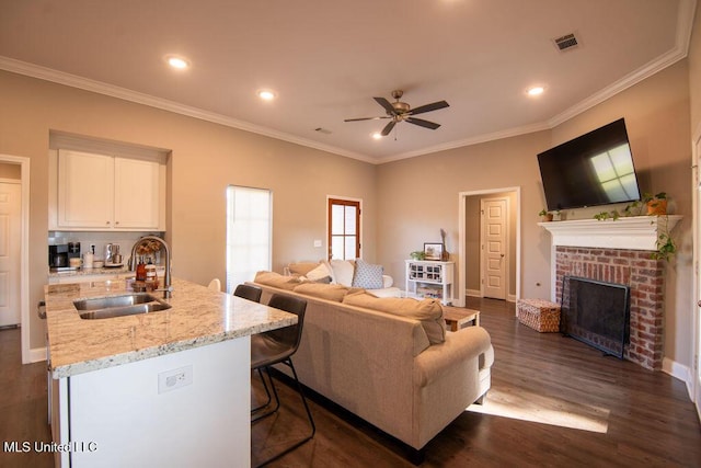 living room with crown molding, dark wood-style flooring, a brick fireplace, a ceiling fan, and visible vents