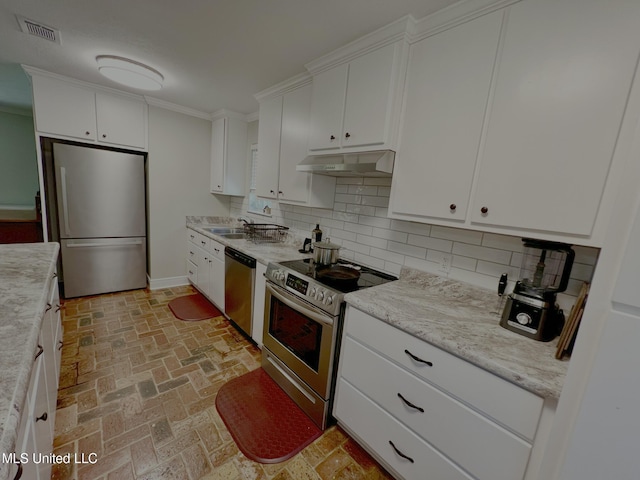 kitchen featuring stainless steel appliances, under cabinet range hood, white cabinetry, brick floors, and tasteful backsplash