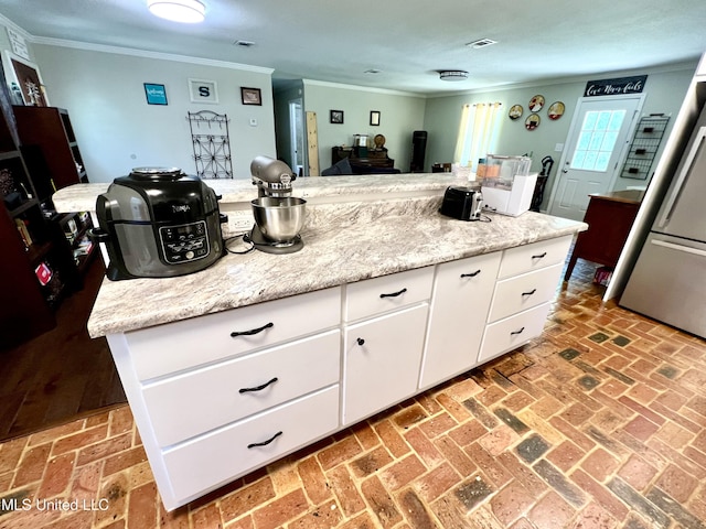 kitchen featuring crown molding, stainless steel fridge, brick flooring, and white cabinets