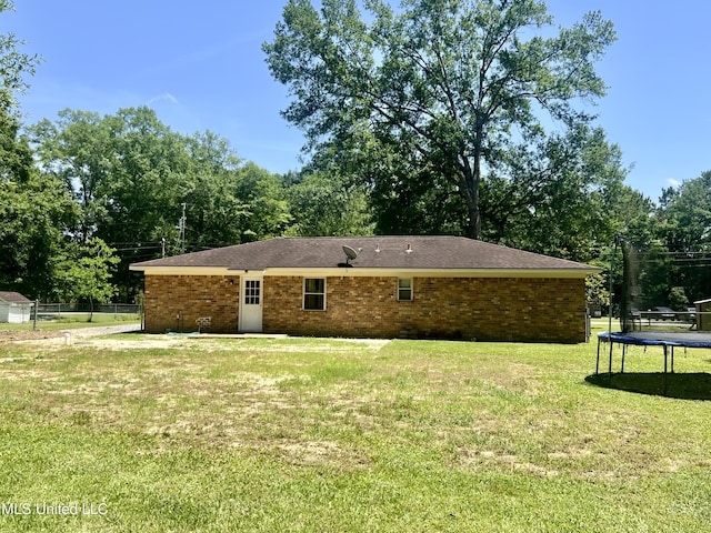 back of property with a trampoline, brick siding, and view of wooded area