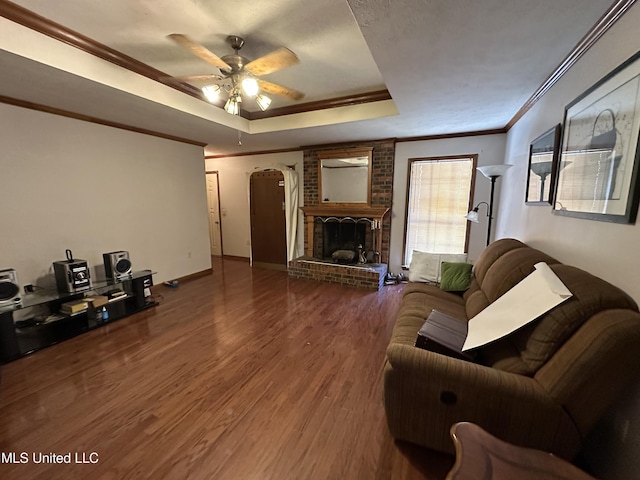 living room with ceiling fan, a raised ceiling, hardwood / wood-style flooring, a fireplace, and ornamental molding