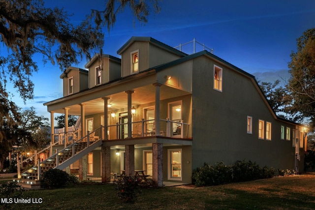 back of property at dusk featuring a lawn, stairway, and a balcony