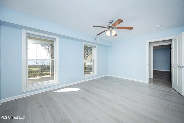 spare room featuring plenty of natural light, wood finished floors, a ceiling fan, and baseboards