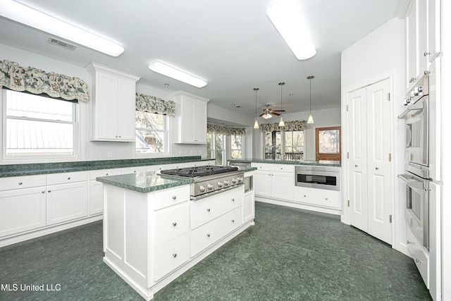 kitchen featuring visible vents, dark floors, a peninsula, stainless steel appliances, and white cabinetry