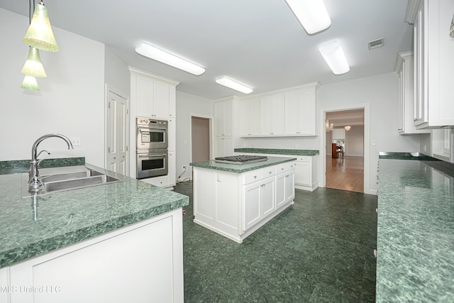 kitchen featuring stainless steel appliances, dark countertops, visible vents, white cabinets, and a sink