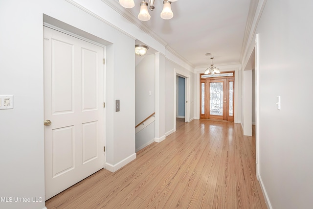 foyer entrance with ornamental molding, light wood-style floors, a notable chandelier, and baseboards