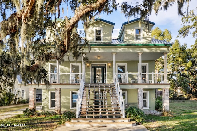 view of front of home featuring a porch, metal roof, stairs, a front lawn, and stucco siding