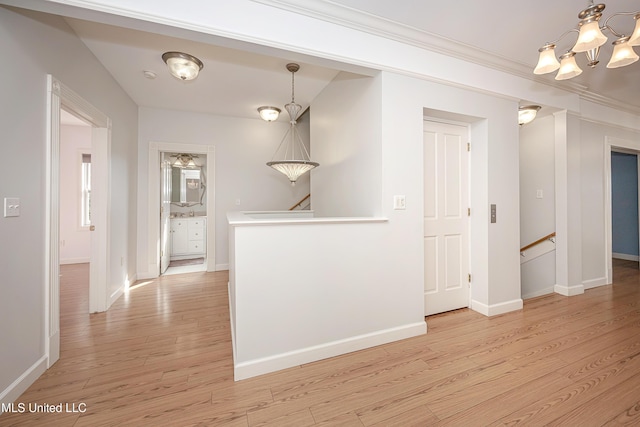 corridor featuring light wood-style floors, baseboards, ornamental molding, and an upstairs landing