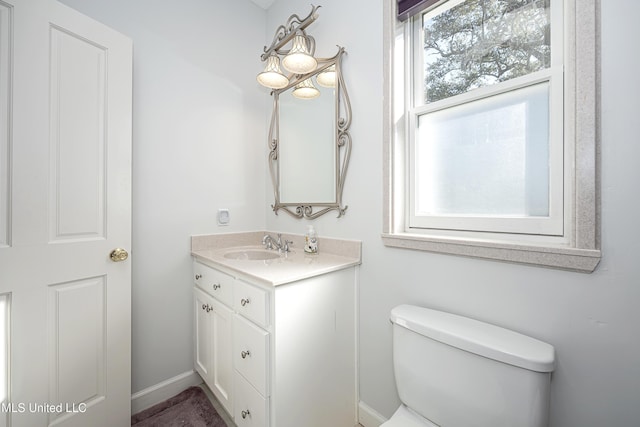 half bath featuring baseboards, vanity, and toilet