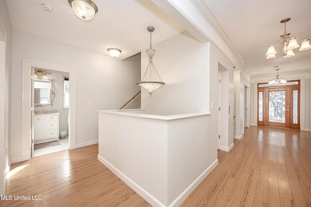 hallway featuring crown molding, light wood finished floors, an upstairs landing, a chandelier, and baseboards