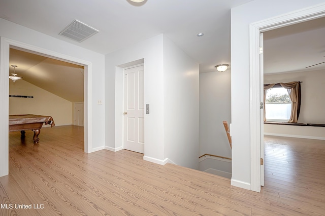 hall featuring baseboards, visible vents, wood finished floors, and an upstairs landing