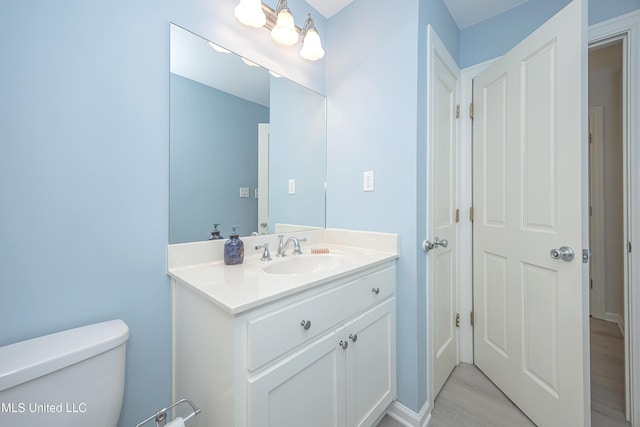 half bathroom with wood finished floors, vanity, and toilet