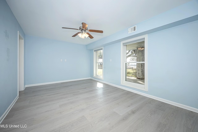 spare room featuring a ceiling fan, visible vents, baseboards, and wood finished floors