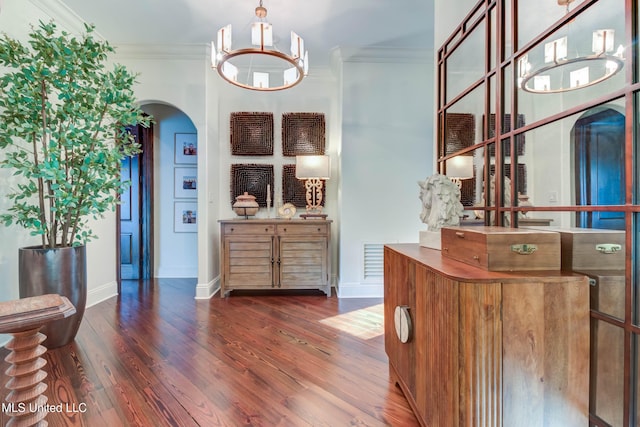 hallway featuring wood finished floors, arched walkways, crown molding, baseboards, and a chandelier