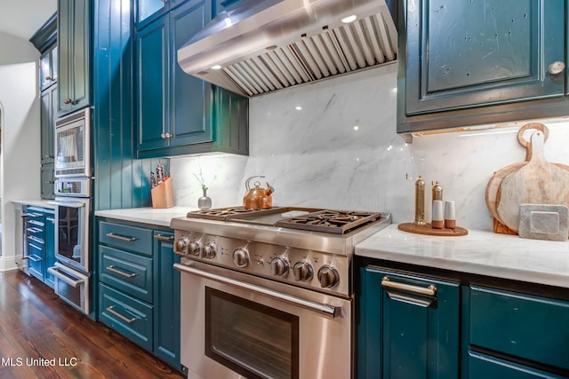 kitchen with a warming drawer, dark wood-type flooring, appliances with stainless steel finishes, wall chimney exhaust hood, and decorative backsplash