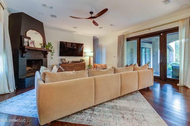 living area featuring visible vents, wood finished floors, crown molding, a brick fireplace, and ceiling fan