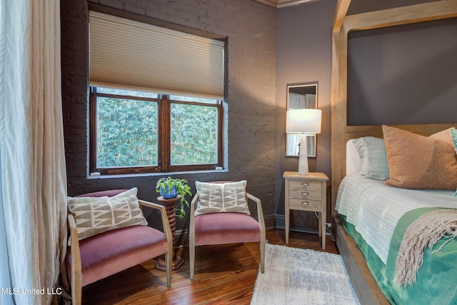 bedroom featuring wood finished floors, baseboards, and brick wall