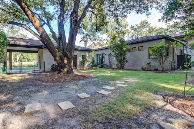 view of front facade featuring stucco siding, a gate, fence, a front yard, and a carport