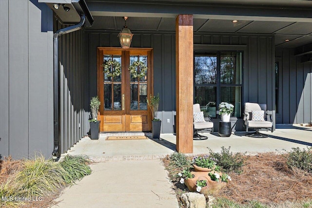 view of exterior entry featuring covered porch, board and batten siding, and french doors