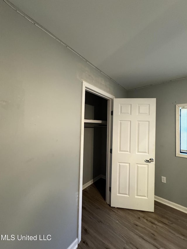 unfurnished bedroom featuring a closet, baseboards, and dark wood-style flooring