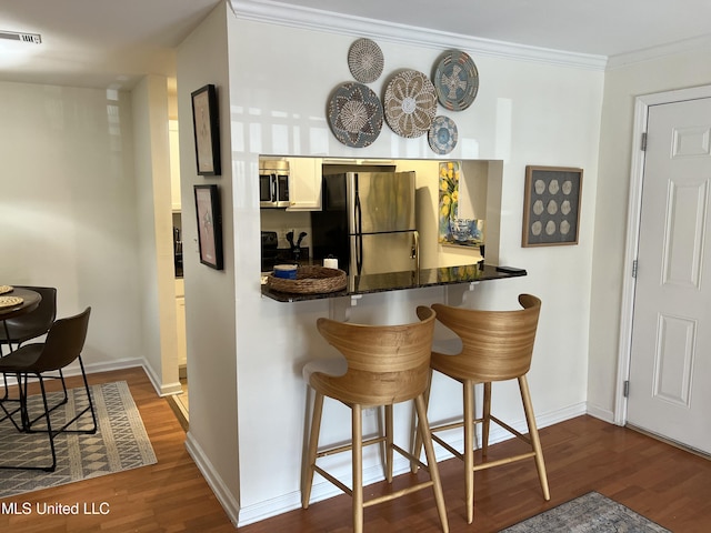 kitchen featuring dark wood-type flooring, crown molding, a kitchen breakfast bar, kitchen peninsula, and stainless steel appliances