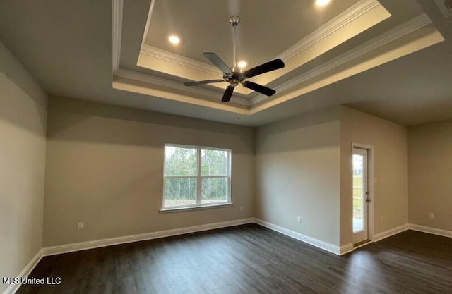 empty room with a tray ceiling, baseboards, ornamental molding, and dark wood finished floors