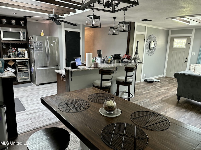 dining area featuring baseboards, a ceiling fan, light wood-type flooring, wine cooler, and a bar