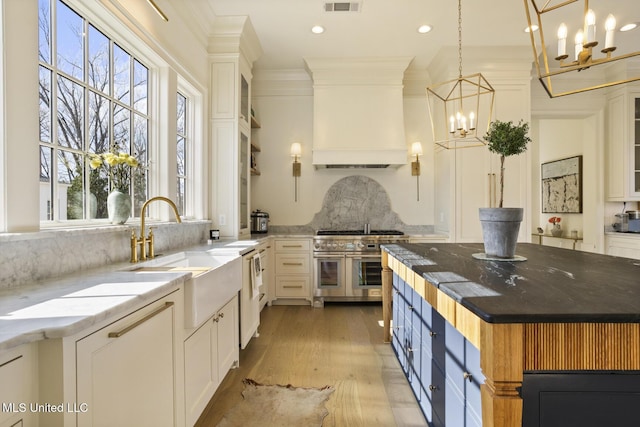 kitchen featuring sink, pendant lighting, dark stone counters, range with two ovens, and white cabinets