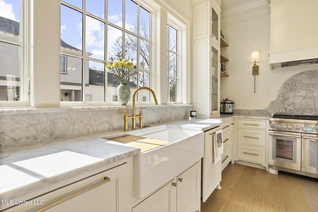 kitchen with light hardwood / wood-style flooring, backsplash, light stone counters, custom range hood, and range with two ovens