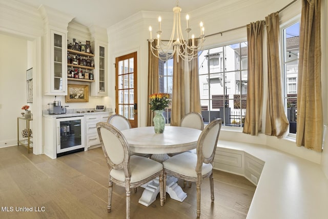 dining room featuring crown molding, a notable chandelier, bar area, beverage cooler, and light wood-type flooring