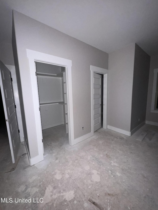 unfurnished bedroom with a closet, a walk in closet, and baseboards