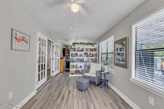 sitting room with french doors, light hardwood / wood-style flooring, a textured ceiling, and ceiling fan