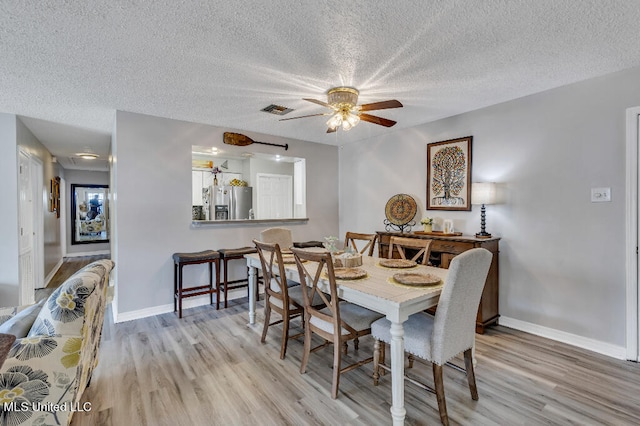 dining space with a textured ceiling, light wood-type flooring, and ceiling fan