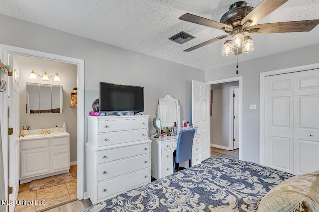 bedroom with a textured ceiling, ensuite bathroom, light wood-type flooring, and ceiling fan