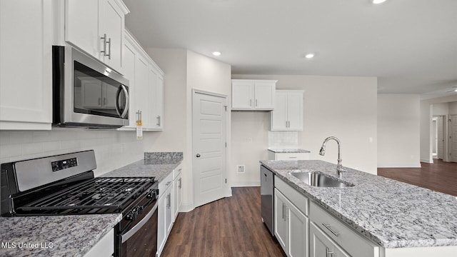 kitchen with appliances with stainless steel finishes, sink, white cabinets, a kitchen island with sink, and light stone counters