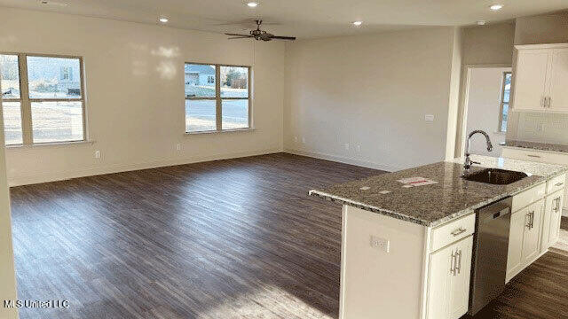 kitchen with sink, white cabinetry, dark stone countertops, stainless steel dishwasher, and an island with sink