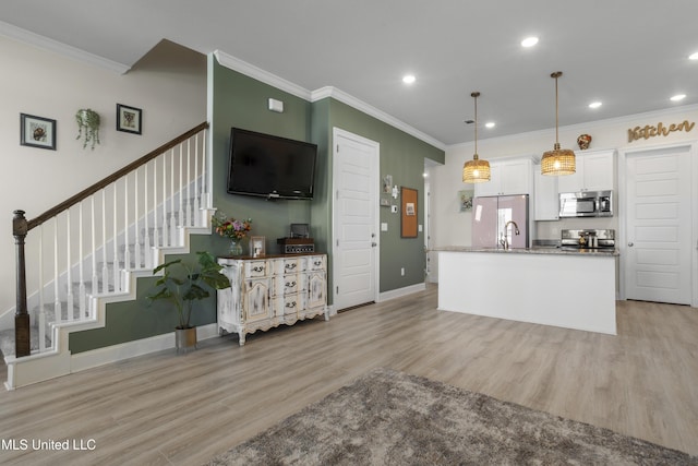 kitchen with light wood finished floors, white cabinets, appliances with stainless steel finishes, ornamental molding, and hanging light fixtures