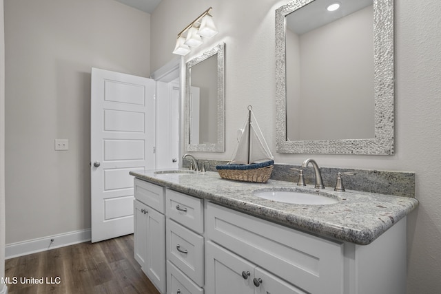 bathroom with double vanity, baseboards, a sink, and wood finished floors