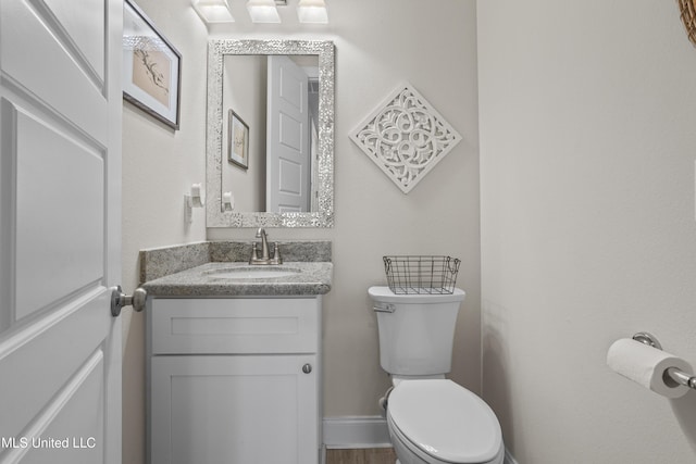 bathroom with toilet, baseboards, wood finished floors, and vanity