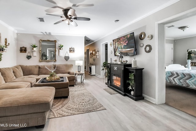 living room with light wood-style floors, crown molding, and a glass covered fireplace