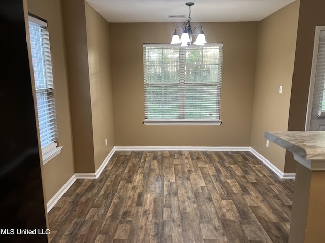 unfurnished dining area with a chandelier, dark wood finished floors, and baseboards